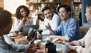Man speaks to a group of people at a table while a man and a woman sit and listen