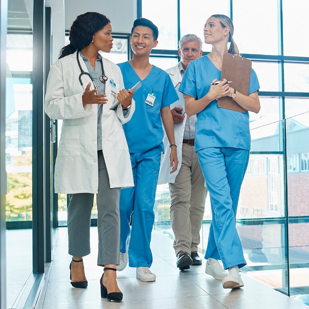 A diverse group of healthcare professionals, including a doctor and nurses, walking and discussing in a bright, modern hospital corridor