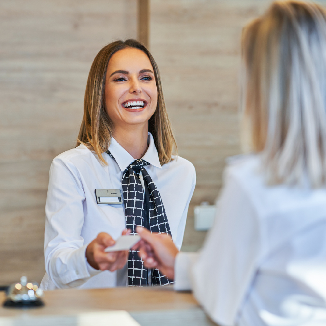 A smiling hotel receptionist in a professional uniform hands a key card to a guest at the front desk.