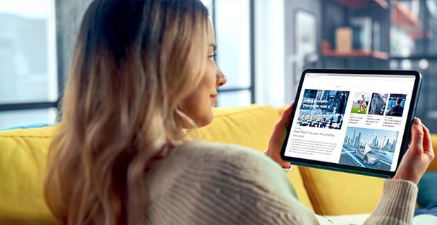 Woman on a yellow couch looking at a tablet screen with several ads